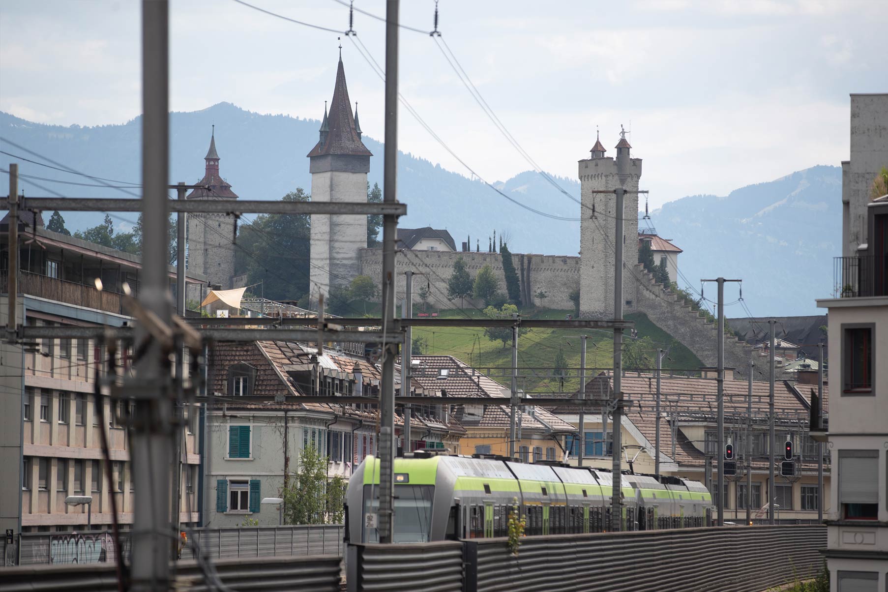 Bild von einem fahrenden grünen Zug durch Luzern. Im Hintergrund sieht man die Museggmauer.